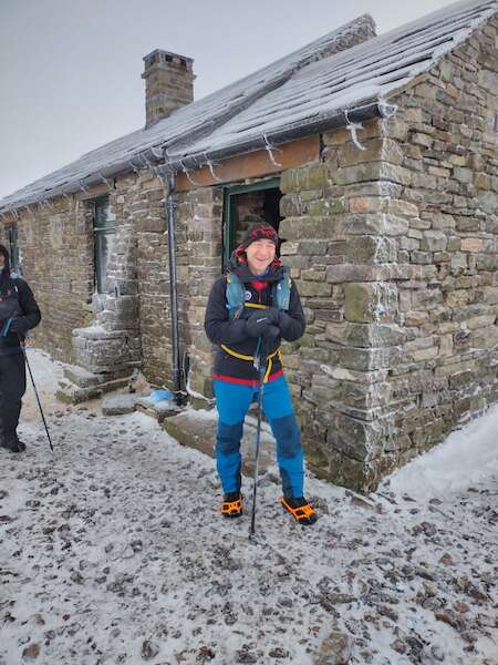 Man standing by a frozen stone bothy with light snow on the ground around him